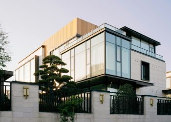 Modernus dviejų aukštų gyvenamasis namas su stiklo fasadu vakaro šviesoje